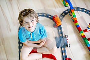 Little blond kid boy playing with colorful plastic blocks and creating train station