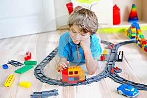 Little blond kid boy playing with colorful plastic blocks and creating train station