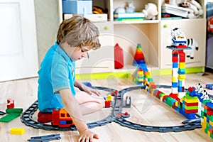 Little blond kid boy playing with colorful plastic blocks and creating train station