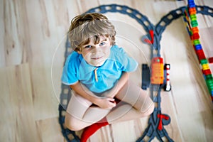 Little blond kid boy playing with colorful plastic blocks and creating train station