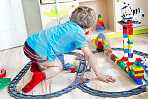 Little blond kid boy playing with colorful plastic blocks and creating train station