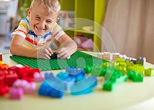 Little blond kid boy playing with lots of colorful plastic block