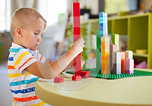 Little blond kid boy playing with lots of colorful plastic block