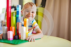 Little blond kid boy playing with lots of colorful plastic block