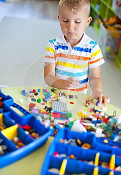 Little blond kid boy playing with lots of colorful plastic block