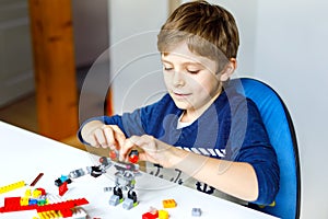 Little blond kid boy playing with lots of colorful plastic blocks.