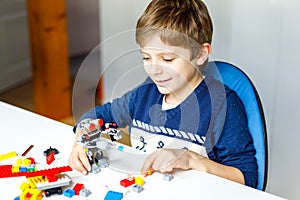 Little blond kid boy playing with lots of colorful plastic blocks.