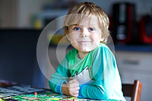 Little blond kid boy playing together board game at home. Funny child having fun