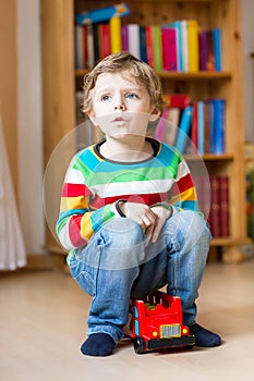 Little blond kid boy playing with wooden toy bus, indoors