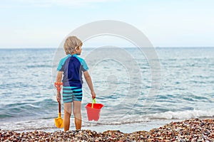 Little blond kid boy standing on lonely ocean beach