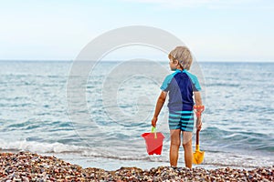 Little blond kid boy standing on lonely ocean beach