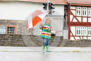 Little blond kid boy walking with big umbrella outdoors