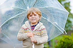 Little blond kid boy walking with big umbrella outdoors