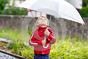 Little blond kid boy walking with big umbrella outdoors