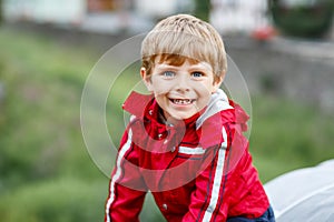 Little blond kid boy walking outdoors on rainy day. Portrait of cute preschool child having fun wear colorful waterproof
