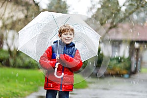 Little blond kid boy on way to school walking during sleet, rain and snow with an umbrella on cold day