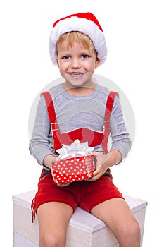 Little blond kid in red costume of dwarf holding gift box with ribbon. Christmas