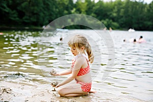 Little blond preschool girl having fun with playing with sand on lake on summer day, outdoors. Happy child learning