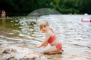 Little blond preschool girl having fun with playing with sand on lake on summer day, outdoors. Happy child learning