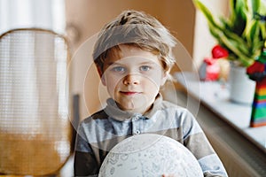 Little blond preschool kid boy with air balloon ball playing indoors at home or nursery. Funny child having fun alone