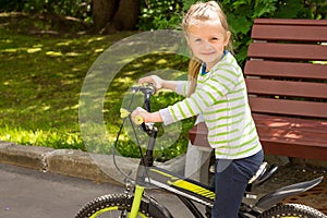 Little blond smiling girl sits on a children`s bike and holds the wheel.