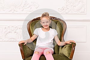 Little blond smiling girl sits in green armchair