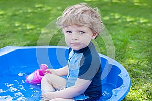 Little blond toddler boy playing with water in summer