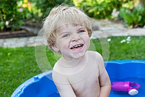 Little blond toddler boy playing with water in summer