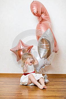 Little blonde baby girl two years old with big pink and white balloons on her birthday party