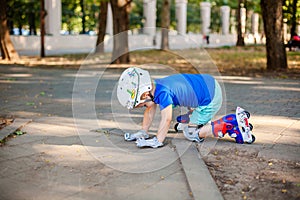 Little blonde boy 3 years old in white sport helmet and blue t-shirt riding on the roller-slates in the summer green park. Special