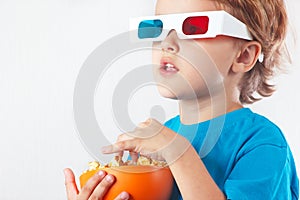 Little blonde boy in 3D glasses with bowl of popcorn
