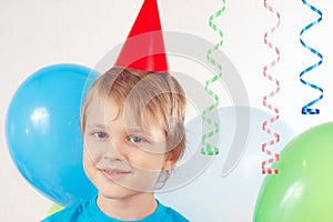 Little blonde boy in festive cap with holiday balls and streamer