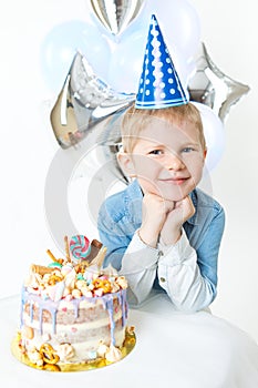 Little blonde boy in festive cap, sit near bithday cake. Concept celebration