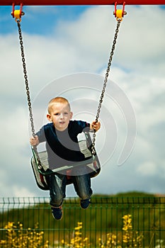 Little blonde boy having fun at the playground. Child kid playing on a swing outdoor.