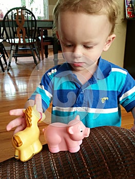 Little blonde boy playing with plastic silicone animals.
