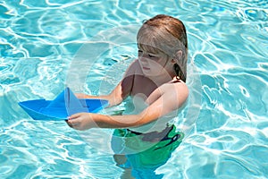 Little blonde boy put paper boat in the sea waves at the beach during summer vacation. Childhood and summer family