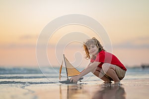 Little blonde boy put toy boat in the sea waves at the beach during summer vacation. Childhood and summer family