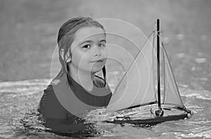 Little blonde boy put toy boat in the sea waves at the beach during summer vacation. Childhood and summer family