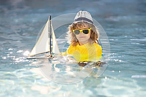Little blonde boy put toy boat in the sea waves at the beach during summer vacation. Summer with kids vacation. Dream on