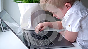 Little blonde boy typing on keyboard notebook computer. press finger on buttons. Digital educations. Computer technology