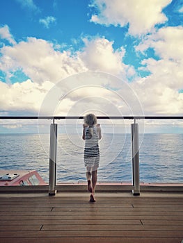 Little blonde Caucasian girl standing on cruise ship deck and looking out on sea ocean. Travelling with kids on cruise liner. View