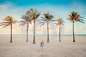 Little blonde Caucasian girl walking on empty Hollywood ocean beach in Florida. Child among tall palm trees on summer sunny day at