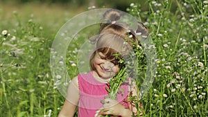 Little blonde child girl in pink dress stay on flower chamomile grass meadow. Bouquet of daisies