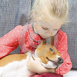 Little blonde curly girl hugging a red basenji dog.