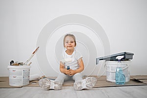 Little blonde cute girl with wall paint roller sitting on the floor