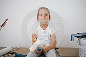 Little blonde cute girl with wall paint roller sitting on the floor