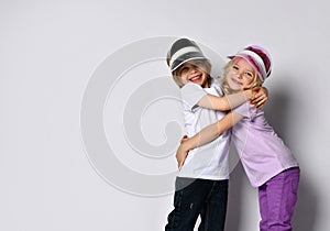 Little blonde female and male in colorful casual clothes and sun visors. Smiling, hugging each other, posing isolated on white