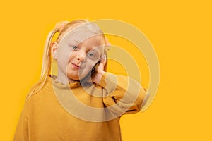 Little blonde girl 4-5 years old use mobile cell phone. Studio portrait of kid wearing yellow sweatshirt on yellow background