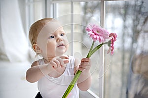 1 little blonde girl with beautiful blue eyes sitting by the window with pink flowers