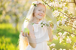 Little blonde girl in blossom apple tree garden